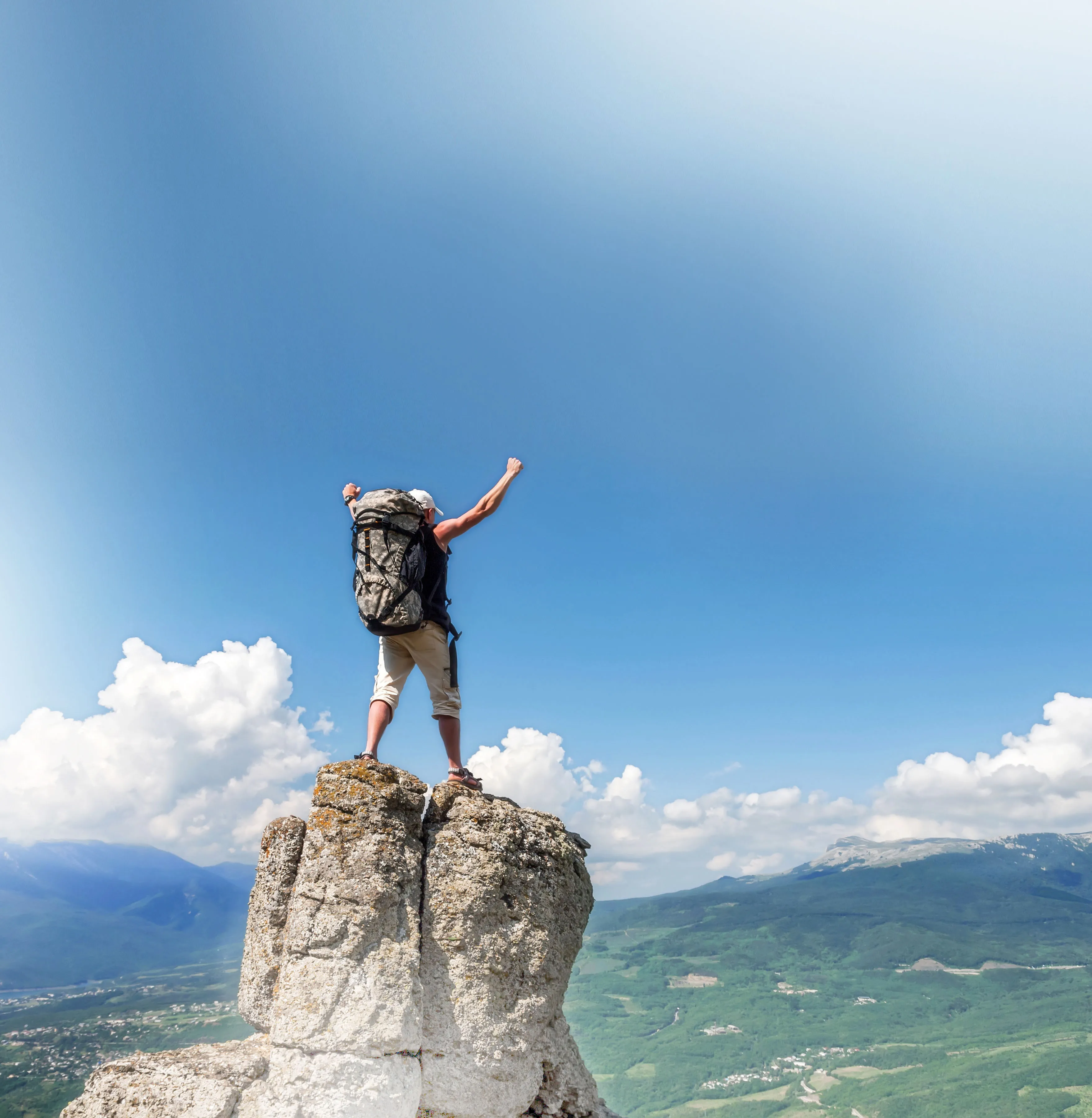A hiker with a backpack stands on a rocky summit above the clouds, one arm raised